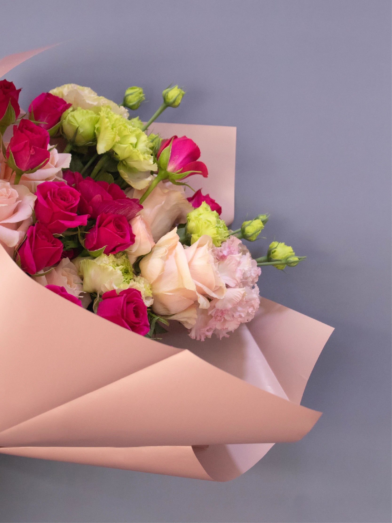 Bouquet of flowers wrapped in pink paper on a gray background.