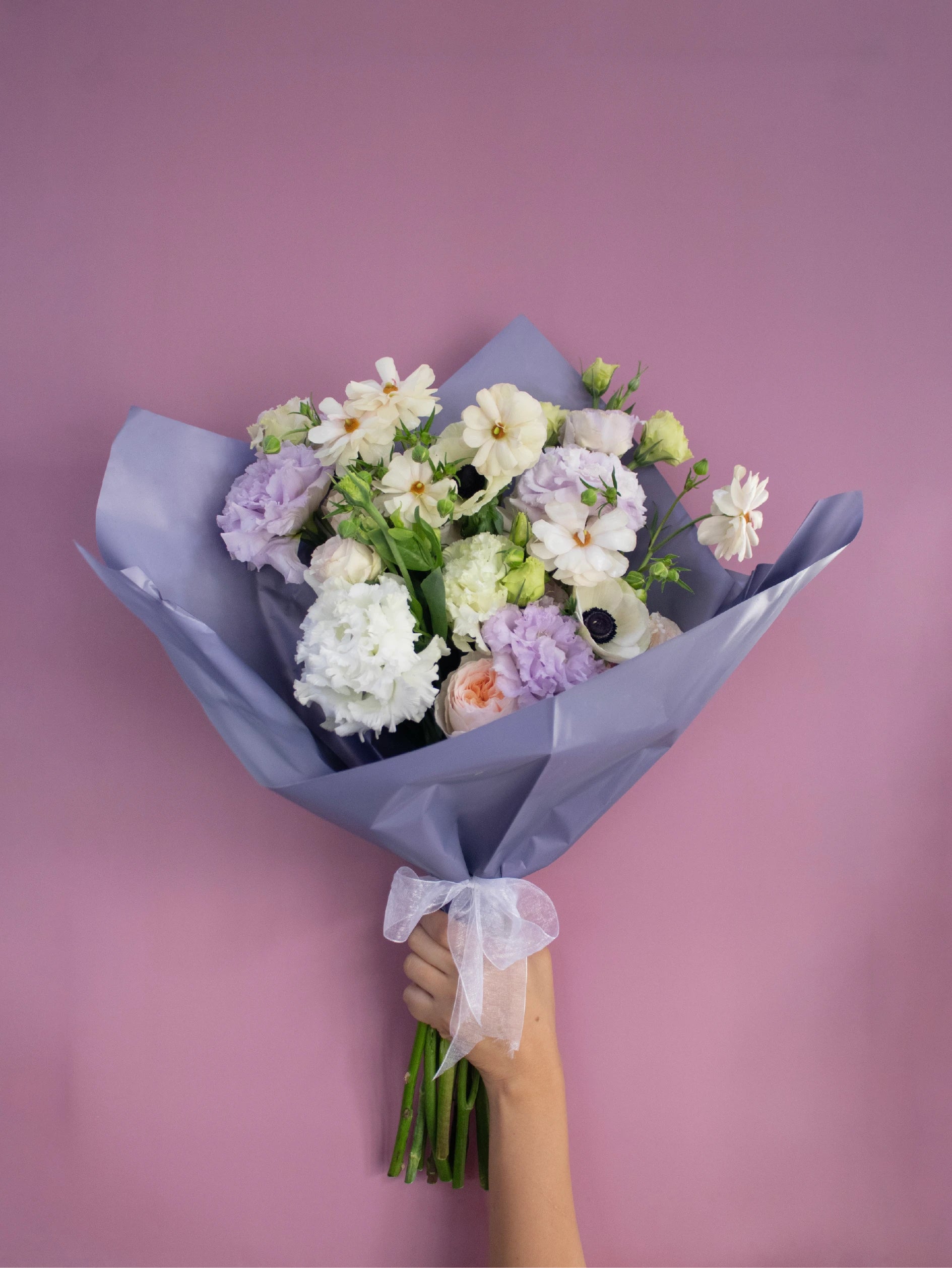 Bouquet of flowers held against a pink background.
