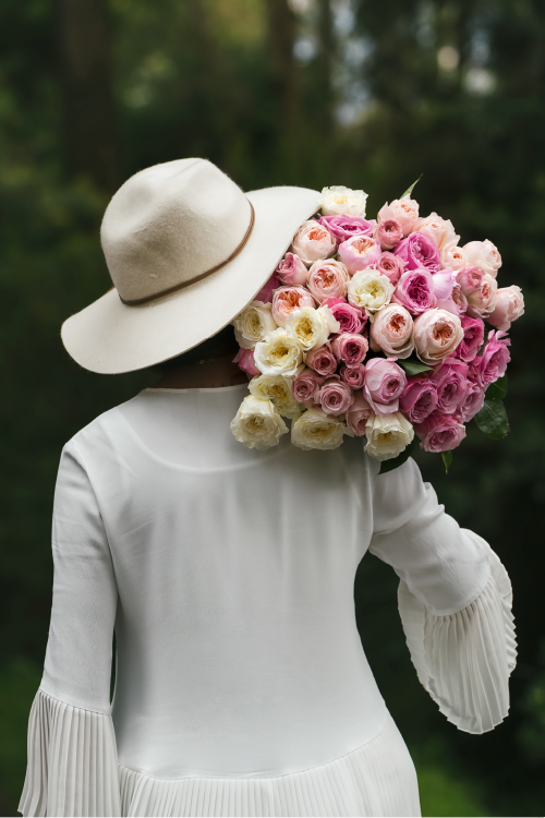 Person wearing a white hat and holding a large bouquet of pink and white garden roses against a blurred natural background.
#color_garden #detail