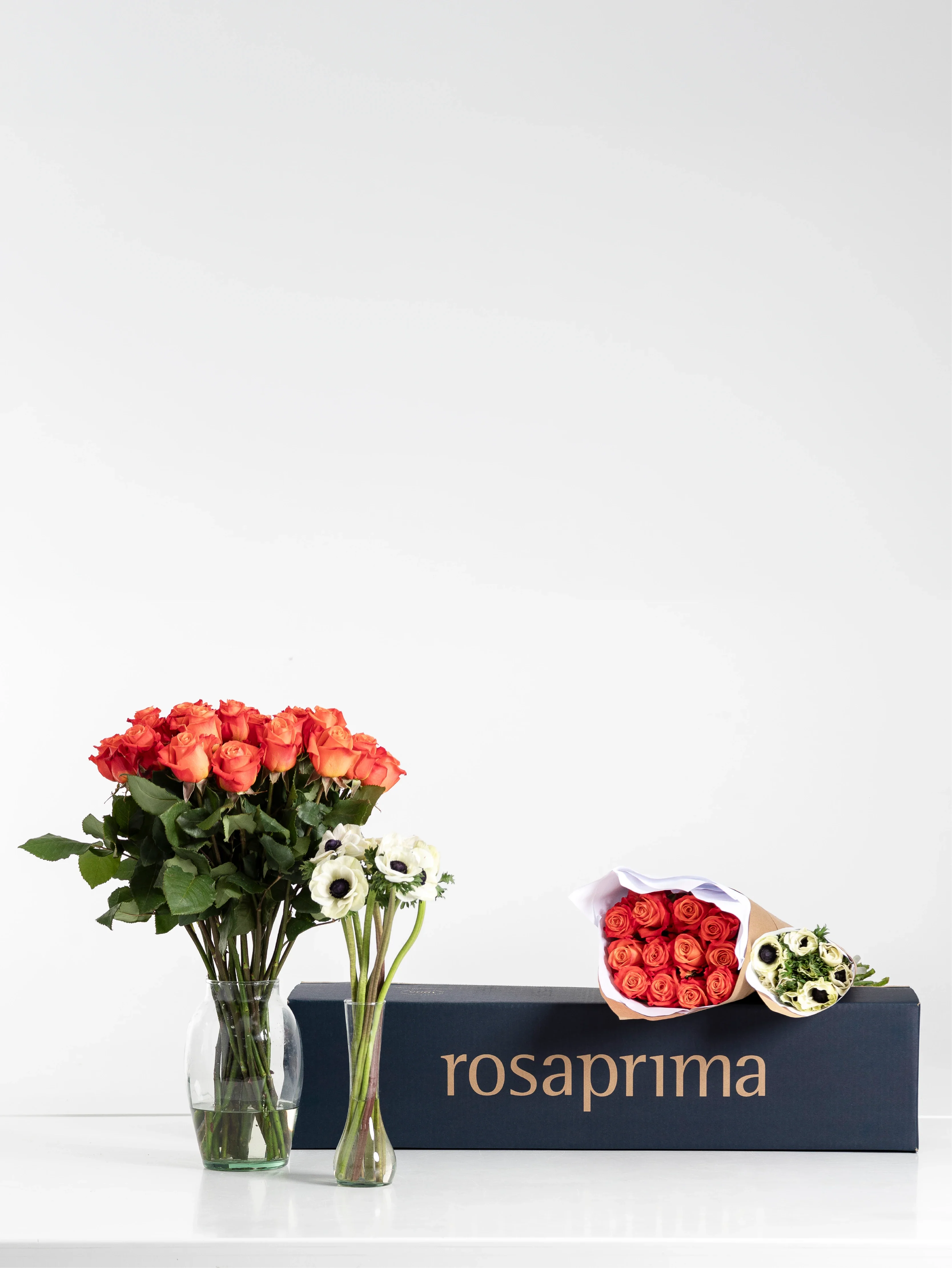 Bouquets of orange standard roses and white mistral anemones with a 'rosaprima' box on a white background.