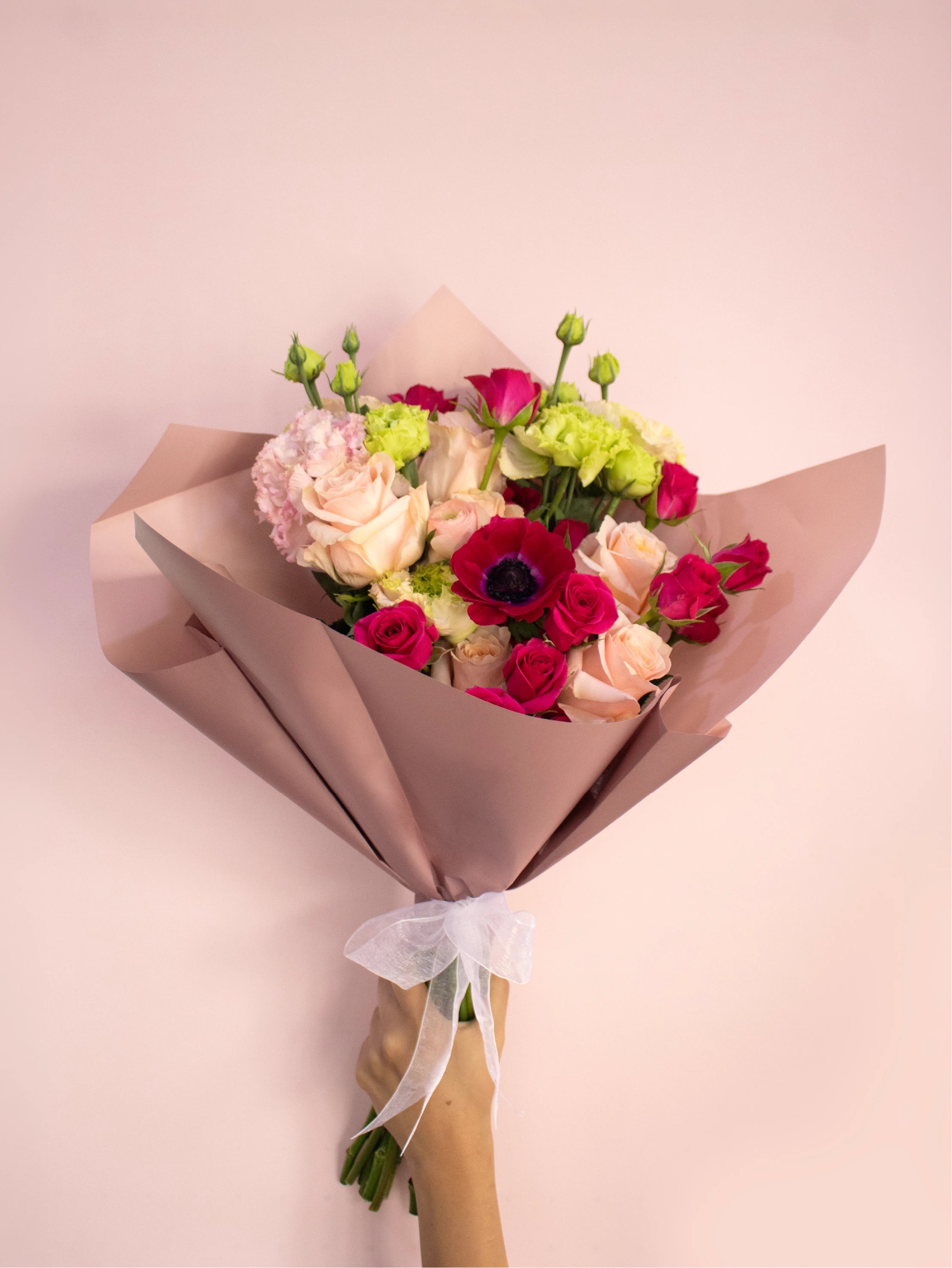 Bouquet of flowers wrapped in pink paper with a white ribbon on a light pink background.