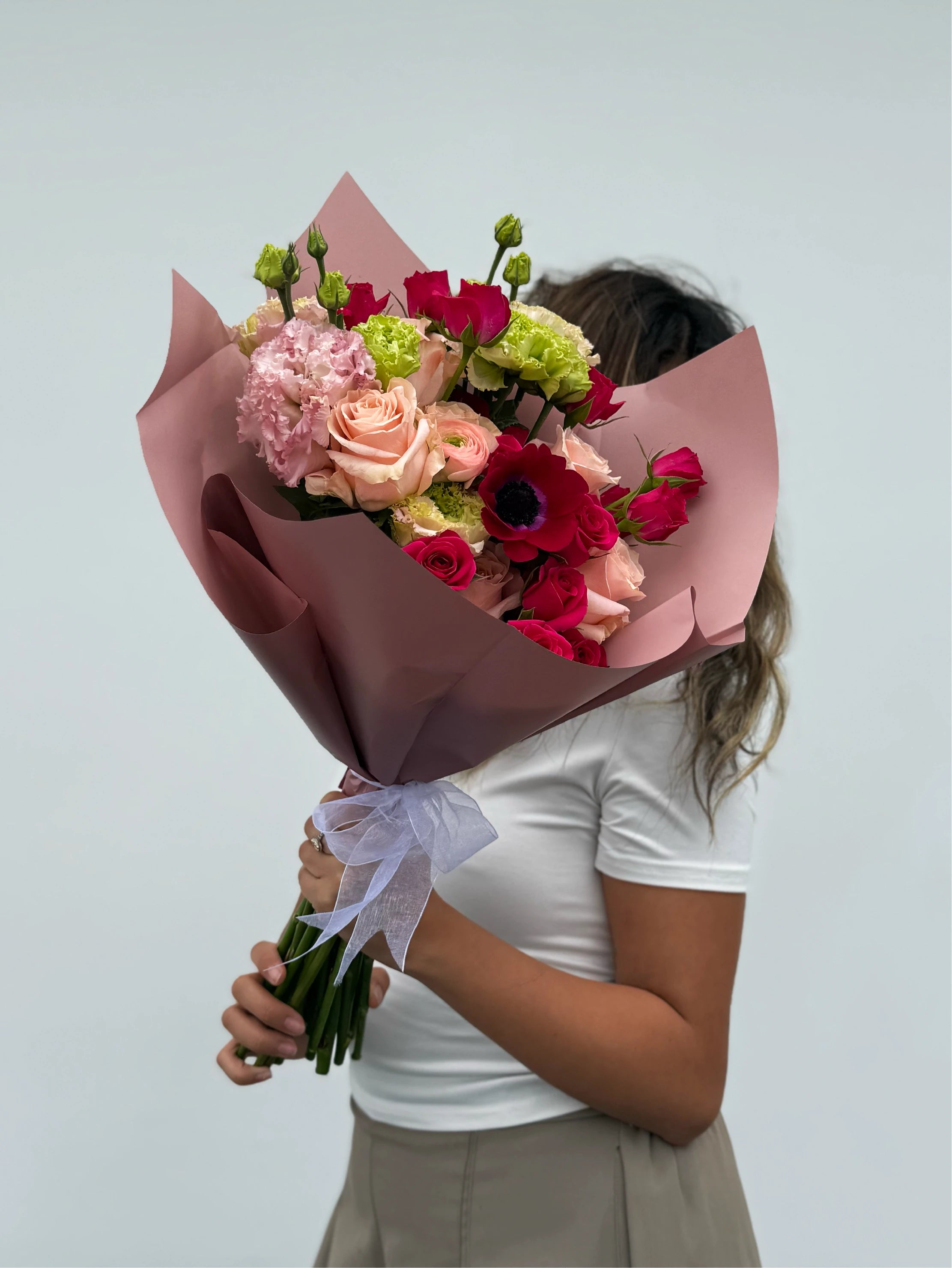 Person holding a bouquet of flowers wrapped in brown paper against a light gray background.
