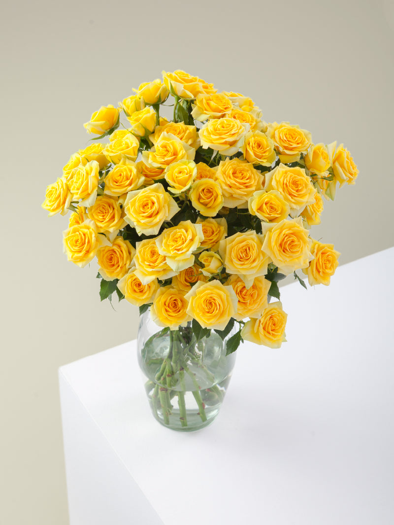 Bouquet of yellow spray roses arranged in a glass vase on a light background.

#color_yellow